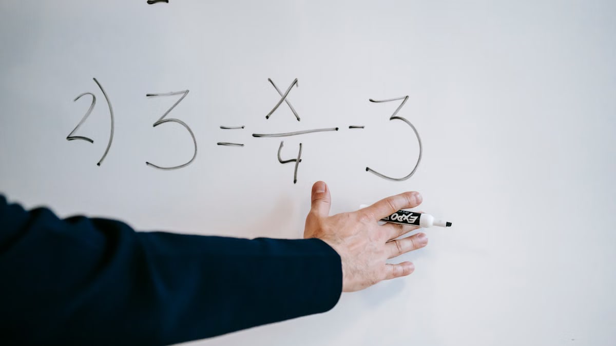 A hand writing a mathematical equation on a whiteboard with a marker.